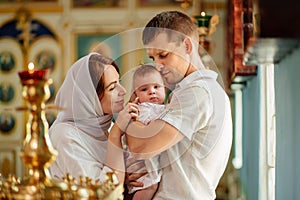 man and woman with baby son in light-colored robes by window in church.
