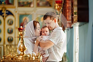 Man and woman with baby son in light-colored robes by window in church.