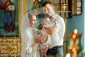 man and woman with baby son in light-colored robes by window in church.