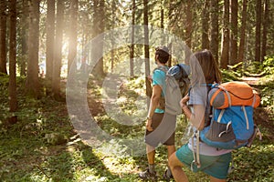 Man and woman with backpack walking on hiking trail path in forest woods during sunny day.Group of friends people summer