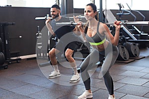 Man and woman with barbell flexing muscles in gym