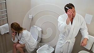 Man and woman in bathrobes are doing their morning routing together in bathroom.