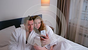 Man and woman in bathrobes making photos on smartphone eating in hotel.