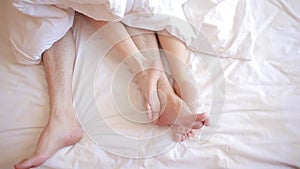 A man and a woman in bed. male and female legs top view, white linens