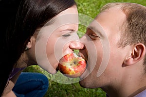 Man and woman bite a red apple