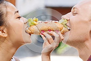 Man and woman biting same hotdog