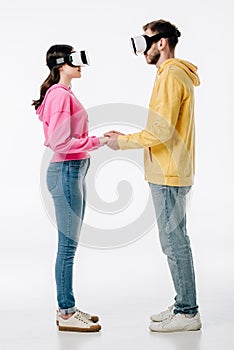 Man in woman in blue jeans and hoodies holding hands while using virtual reality headsets on white background