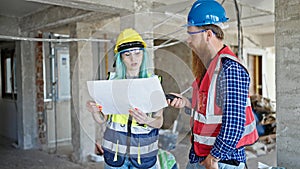 Man and woman builders reading house project speaking by walkie-talkie at construction site