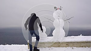 man woman builds snowman on park over sea. Happy family, winter games and outdoor activity. Street entertainment for