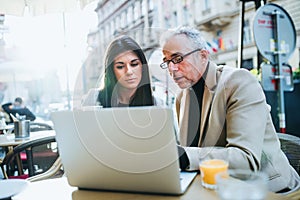 Man and woman business partners with laptop sitting in a cafe in city, talking.