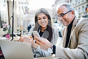 Man and woman business partners with laptop sitting in a cafe in city, talking.