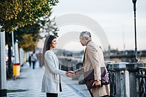 Man and woman business partners standing outdoors in city of Prague, shaking hands.