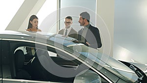 Man and woman buyers talking to car dealership manager discussing automobile