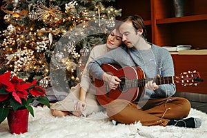 Man and woman celebrating Christmas or New Year holiday together. Man playing guitar and singing for woman. Young couple