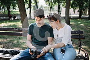 Man and woman checking photos on camera while sitting on bench