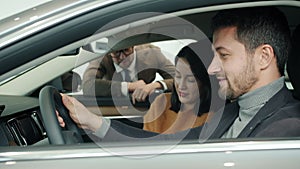 Man and woman with child sitting inside car choosing auto in showroom talking to manager