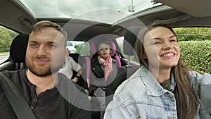 Man and woman with children driving in car, two parents and children traveling and dancing in tre transport. Happy