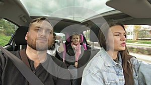 Man and woman with children driving in car, two parents and children traveling and dancing in tre transport. Happy