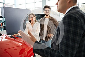 Man and woman choosing new car having consultation with salesman in dealership