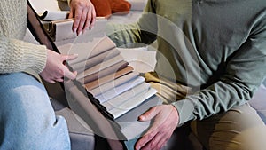 A man and woman choosing upholstery fabric color and texture from various colorful samples for sofa in a store, close up