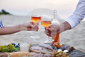 Man and woman clanging wine glasses with rose wine at sunset bea