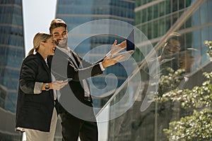 Man and woman in classic suit discussing business details and using laptop while standing outdoors