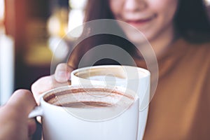 Man and woman clink coffee mugs in cafe