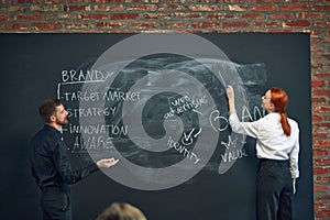 Man and woman, colleagues writing on blackboard marketing strategies of brand development. Building successful business