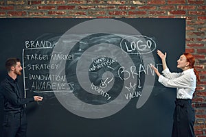 Man and woman, colleagues writing on blackboard marketing strategies of brand development. Building successful business