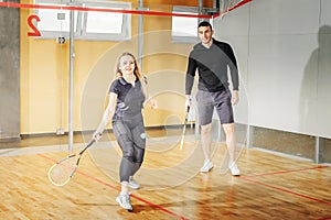 Man and woman compete in a squash game. young guy and girl hold racket