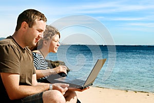 Man and woman with computer at beach