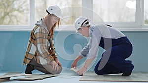 man and woman in construction helmets in process of laying laminate while renovating floor in apartment