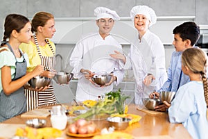 Man and woman cooks, during culinary master class, tell children rules when preparing dough