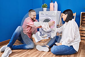 Man and woman couple fighting with clothes at laundry room