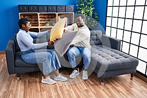 Man and woman couple fighting with cushion sitting on sofa at home