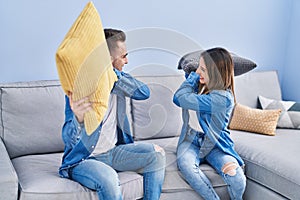 Man and woman couple fighting with cushion sitting on sofa at home