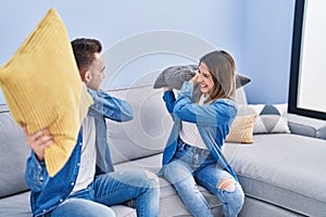 Man and woman couple fighting with cushion sitting on sofa at home