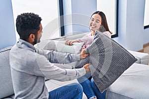 Man and woman couple fighting with cushion sitting on sofa at home