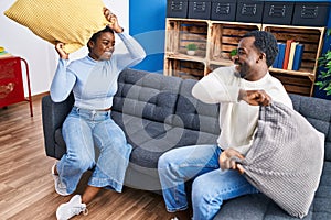 Man and woman couple fighting with cushion sitting on sofa at home