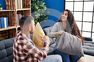 Man and woman couple fighting with cushion sitting on sofa at home
