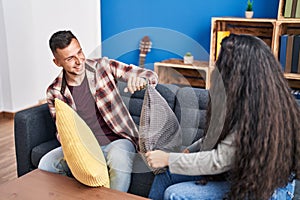 Man and woman couple fighting with cushion sitting on sofa at home