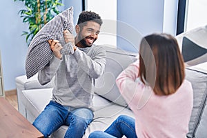 Man and woman couple fighting with cushion sitting on sofa at home