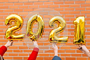 Man and woman couple hands holding gold foil balloons numeral 2021 in front of orange tile bricks. New year celebration concept