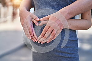 Man and woman couple hugging each other doing heart gesture on belly at street