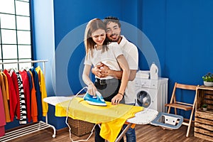 Man and woman couple hugging each other ironing at laundry room