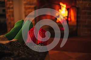 Man and woman, couple in love wearing green and red socks sitting near fireplace, hugging and wrapping in a woolen blanket