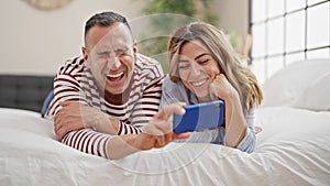 Man and woman couple lying on bed watching video on smartphone at bedroom