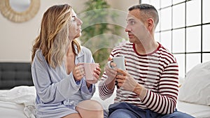 Man and woman couple sitting on bed drinking coffee speaking at bedroom