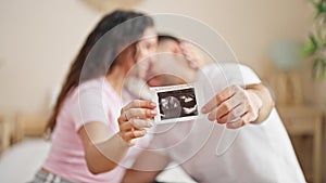 Man and woman couple sitting on bed holding baby ultrasound at bedroom