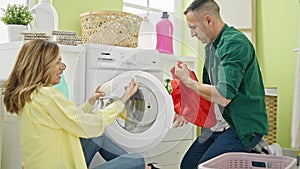 Man and woman couple sitting on floor together smelling dirty clothes at laundry room